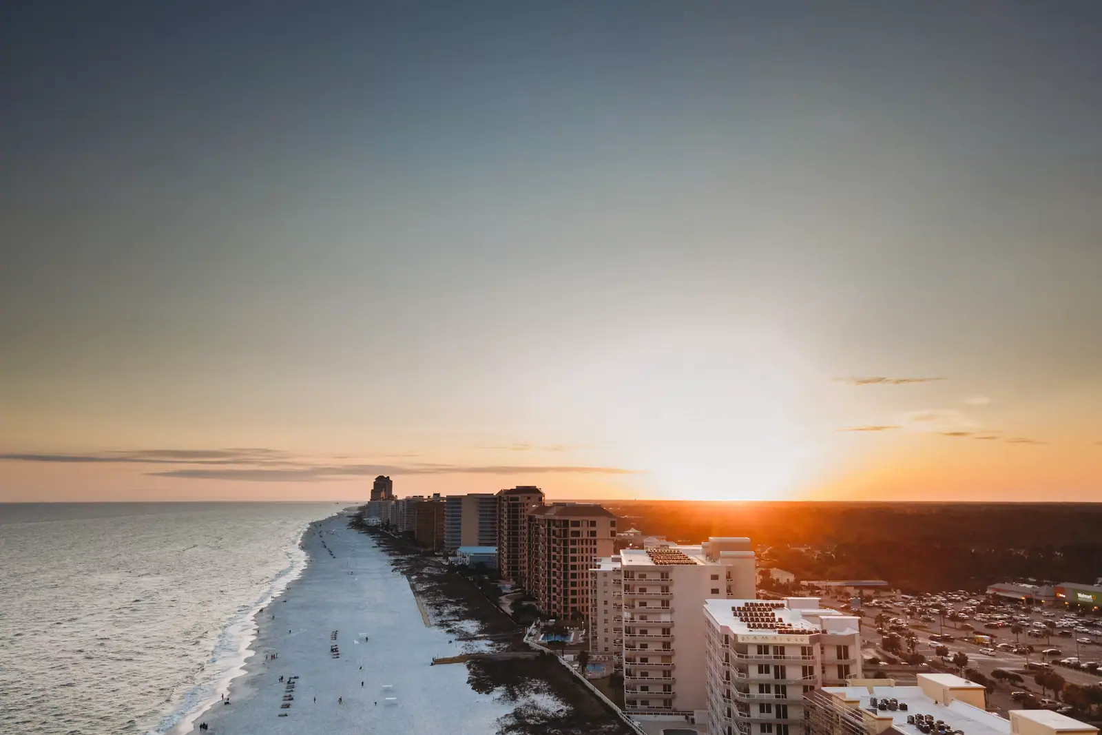 Aerial view at sunset of beachfront condominium towers along a stretch of pale Gulf sand