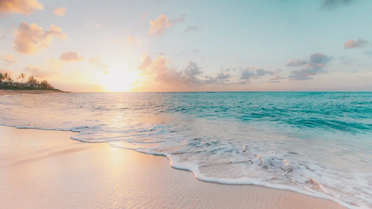 Clear shallow green water meeting a wide stretch of very pale sand under an open sky