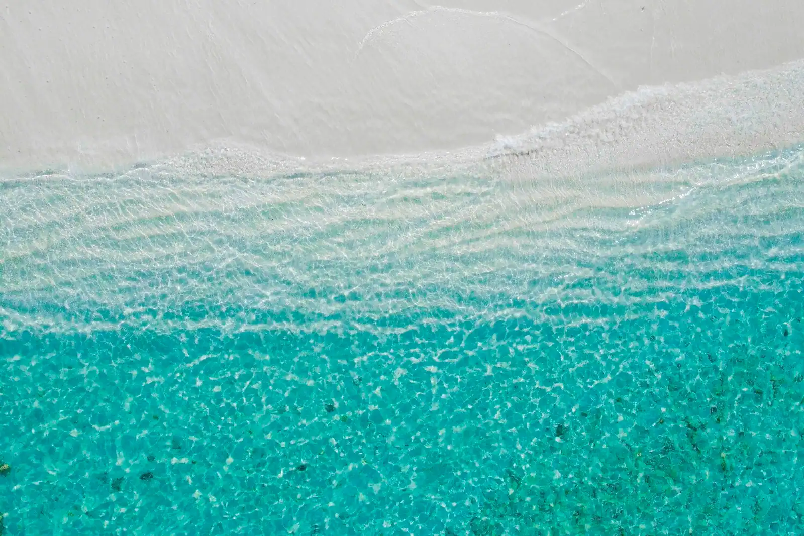 Aerial view of very pale sand meeting clear shallow water shading from green to blue