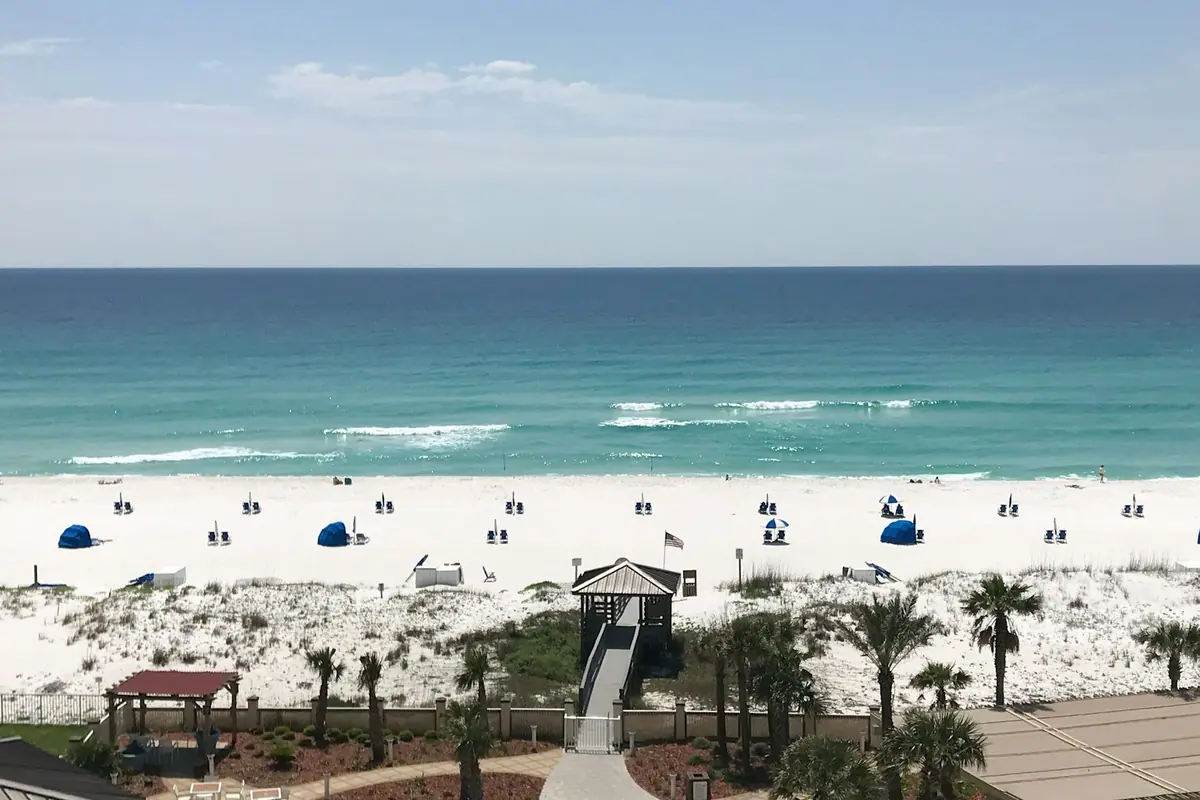 A timber dune walkover leading down to very pale sand with umbrellas and green Gulf water beyond