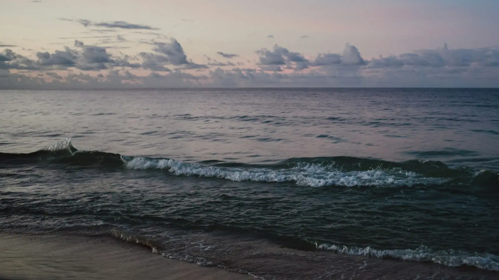 Small waves running up a wide stretch of pale sand under a bright open sky