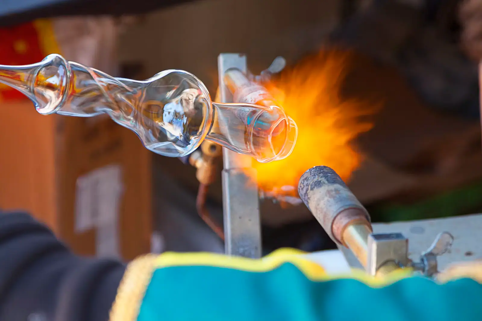 A glassmaker shaping a glowing vase form at the bench