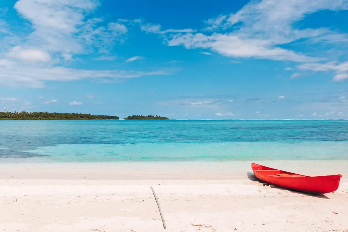 A red kayak resting on sand at the edge of calm shallow water