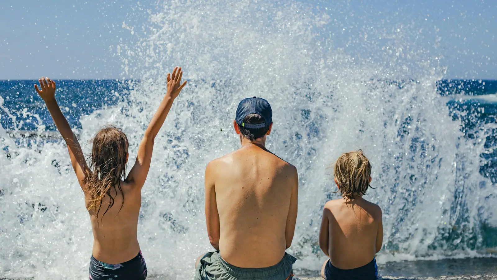 Two children sitting on wet sand at the edge of shallow water on a wide beach