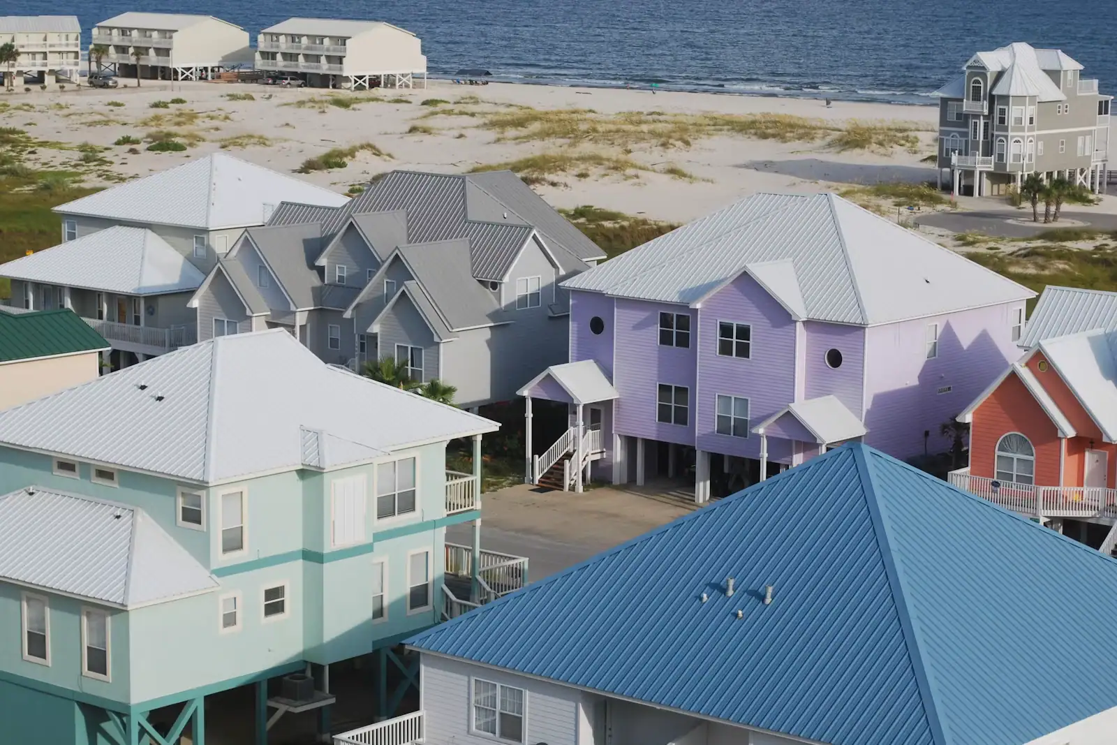 A row of brightly painted raised beach houses standing on a low sandy shoreline