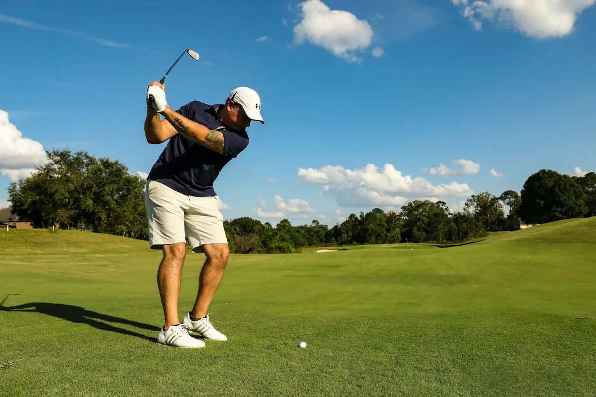 A golfer at the top of the backswing on a sunlit fairway under a blue sky