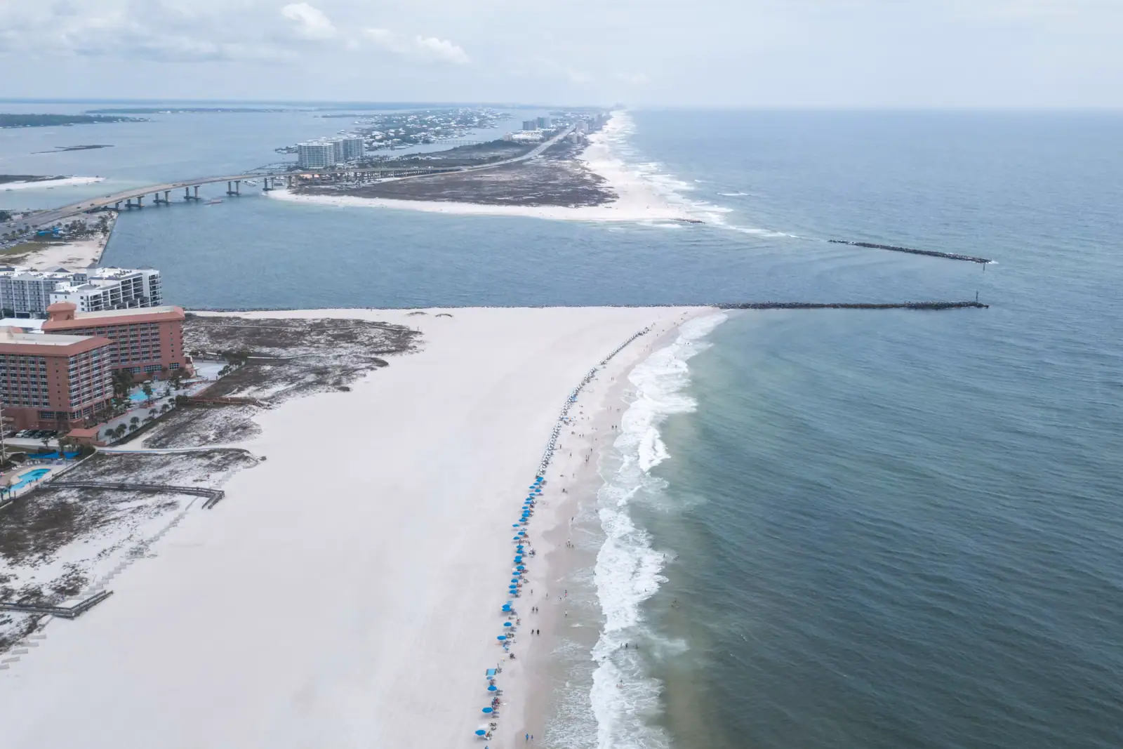 Aerial view of a long straight beach where pale sand meets clear shallow water