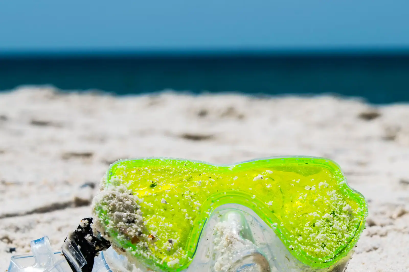 A pair of swimming goggles left on bright white beach sand in strong sunshine