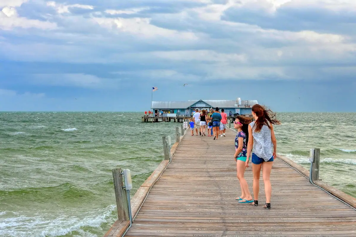 People walking out along a long timber pier over clear green water towards the open sea