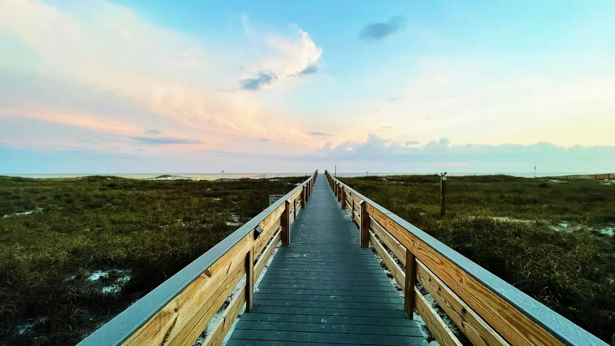 A timber walkway crossing low coastal grass toward open water