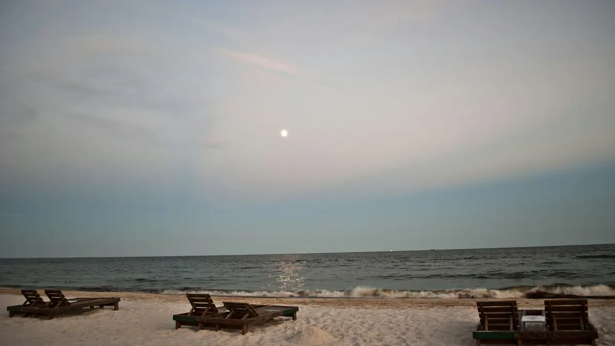 A single sun lounger on an empty stretch of pale sand near the shoreline