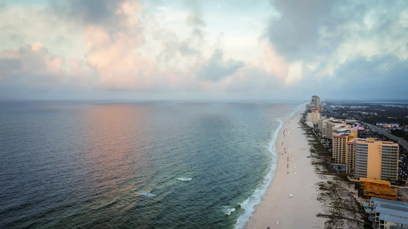 Aerial view of a long sandy beach with a line of low-rise and high-rise buildings behind it