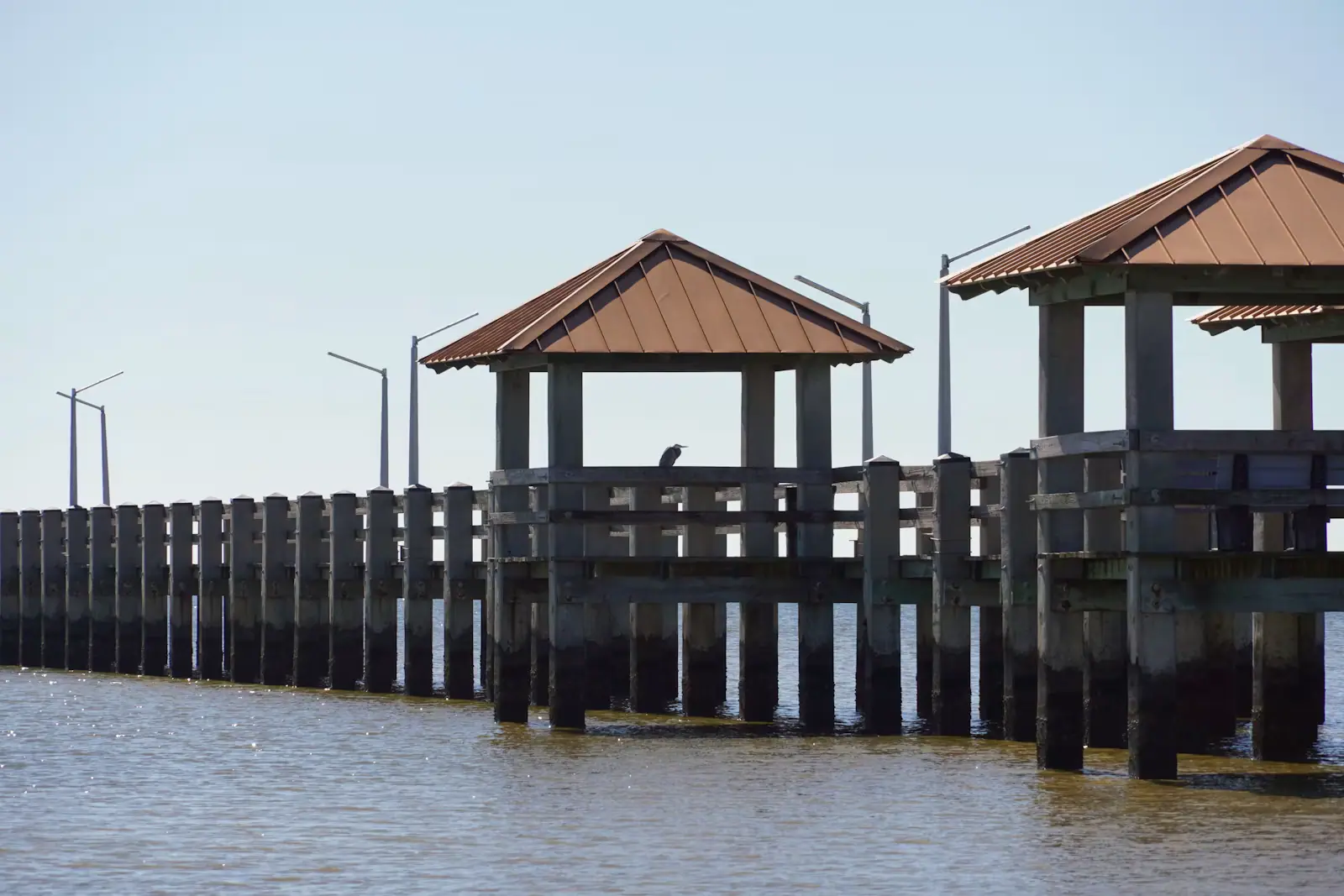 A long low fishing pier with covered shelters running out over still bay water