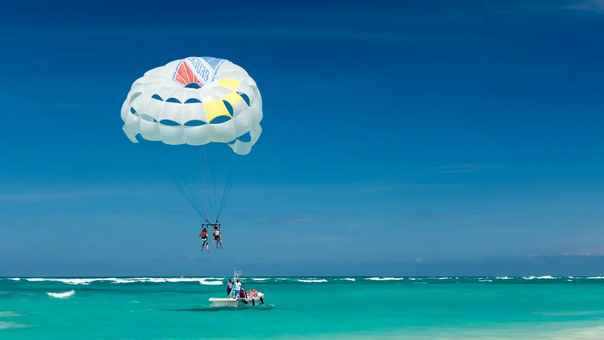 Two people suspended under a parasail canopy above the sea near a beach