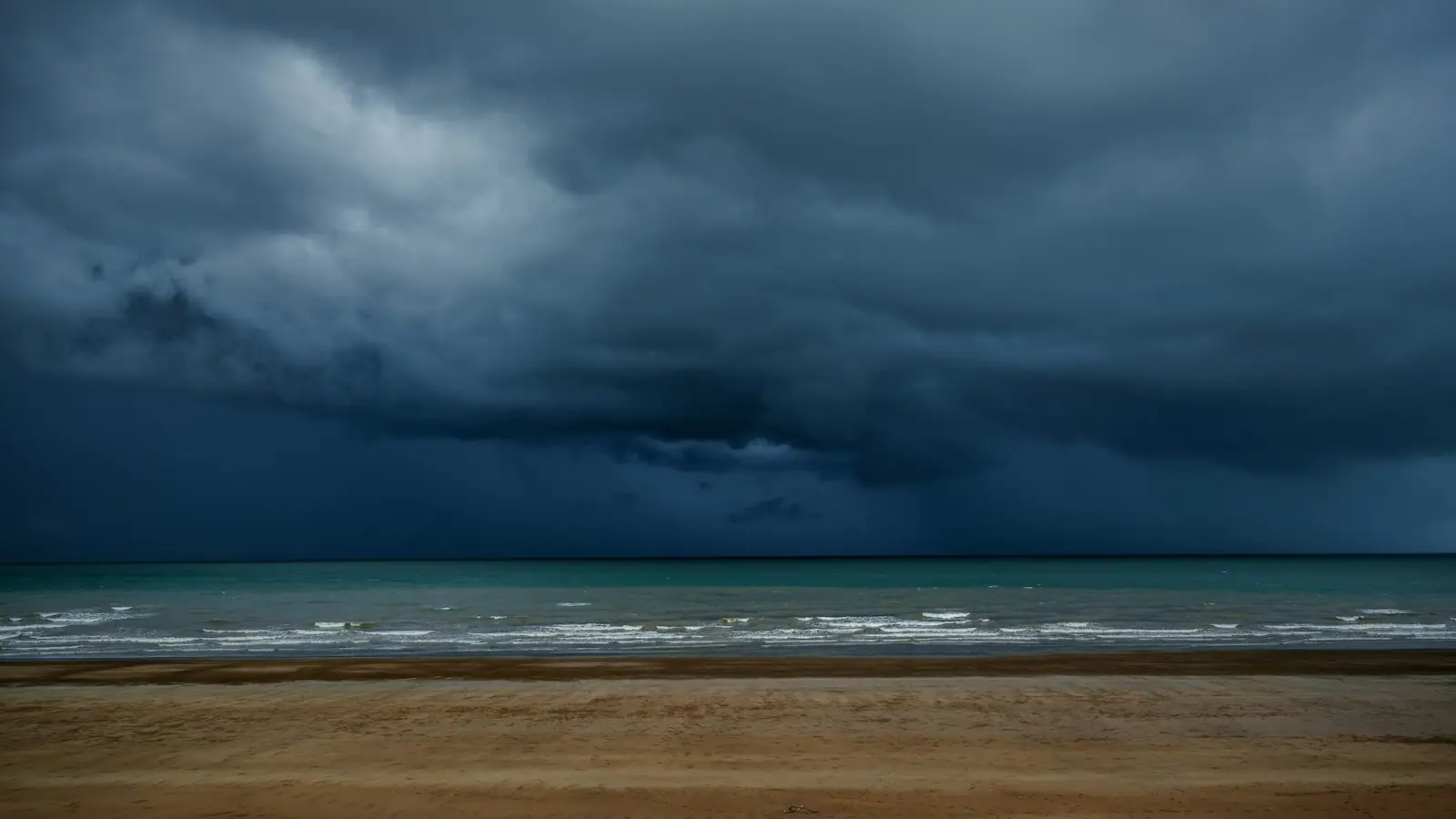 Dark storm cloud building over a flat sea above an empty stretch of beach
