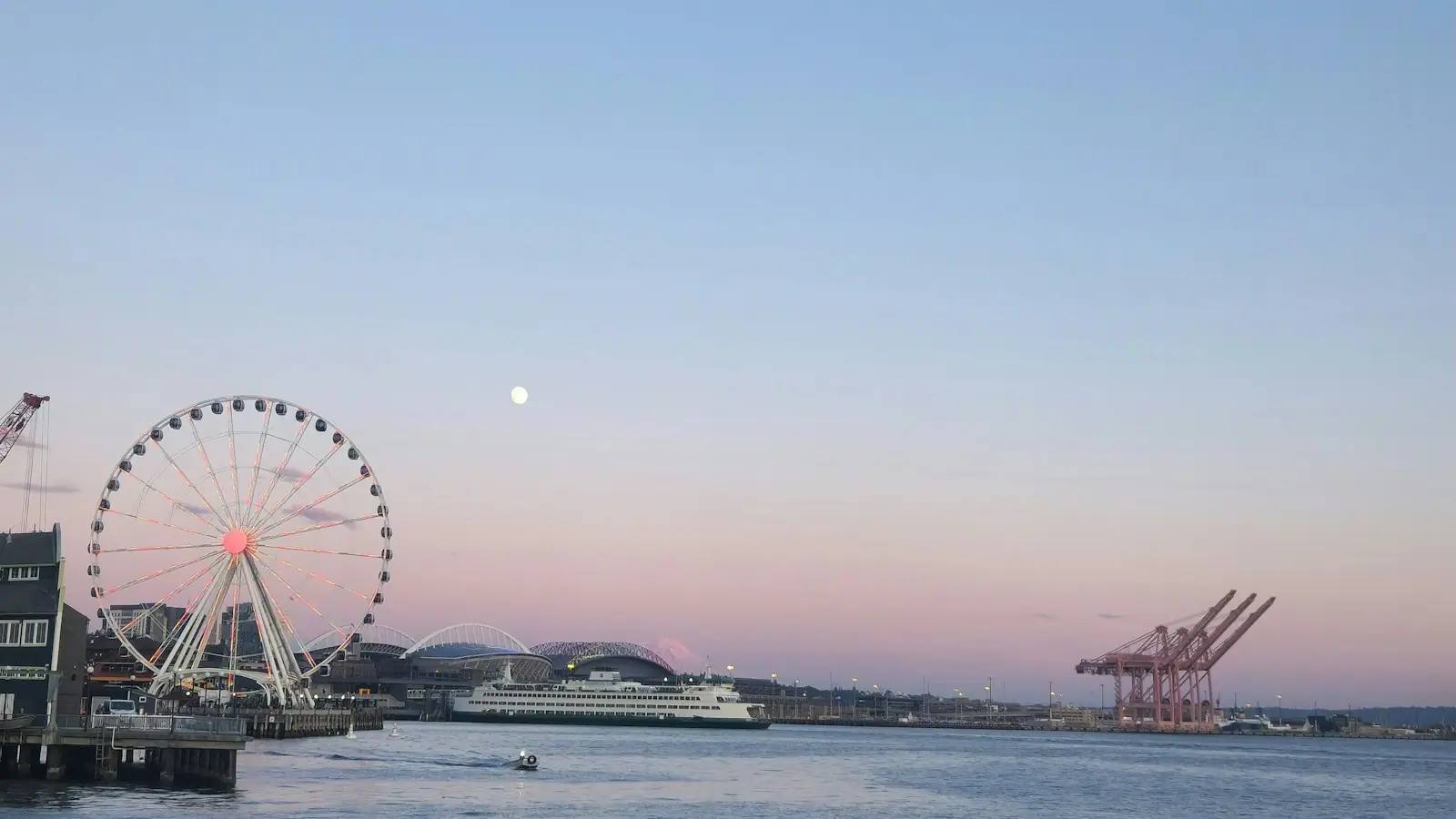 A large Ferris wheel standing beside a body of water at dusk