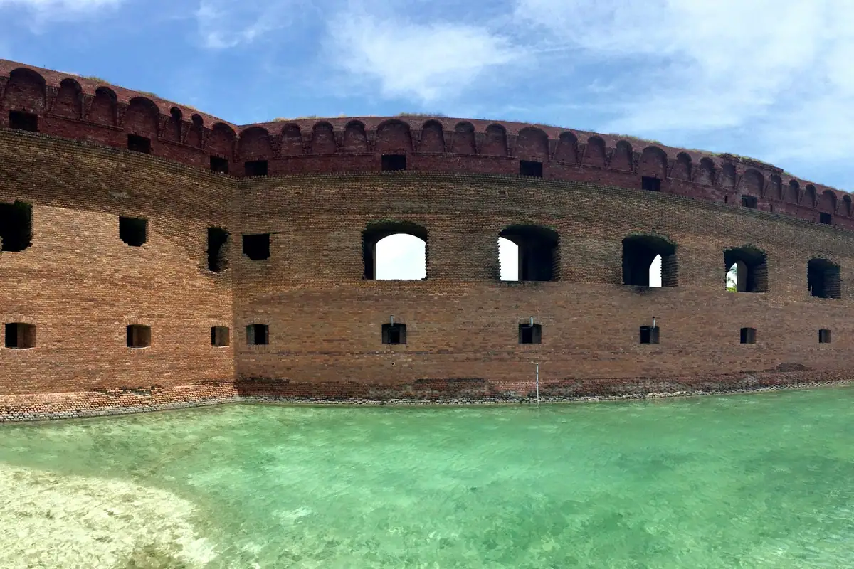 A low historic brick fortification standing at the edge of calm coastal water
