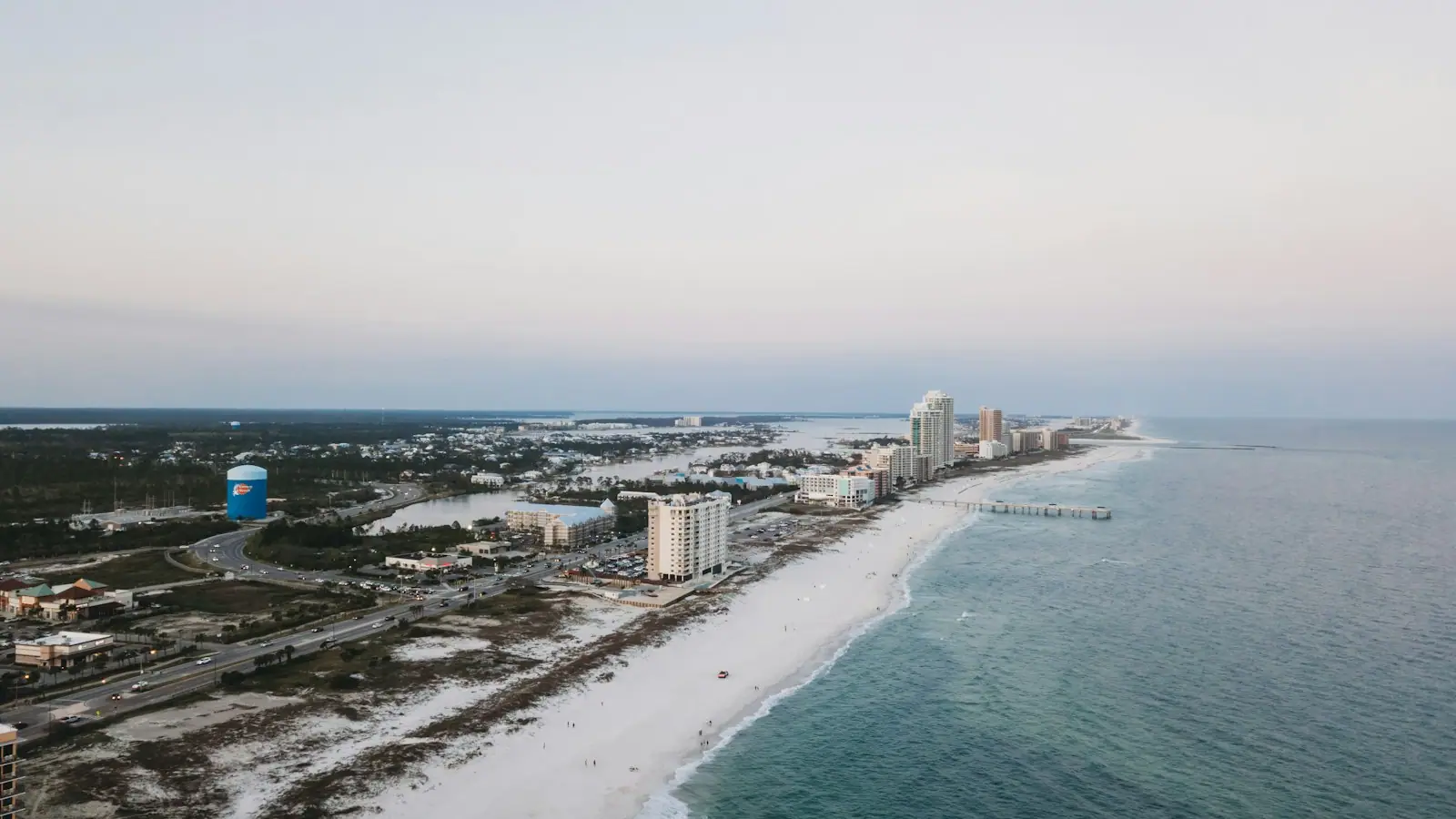 Aerial view of high-rise condominium towers lined along a white sand beach beside shallow green water