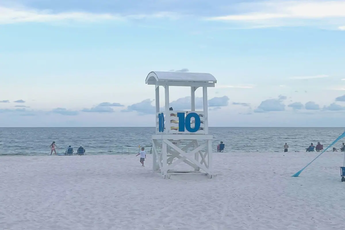 A wooden lifeguard stand on an empty stretch of pale sand under a bright sky