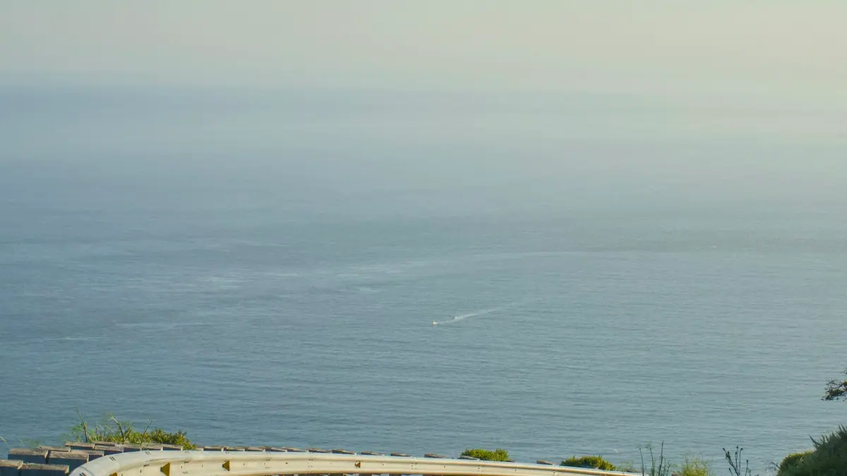 A two-lane road curving along a coastline with open water visible beyond the shoulder