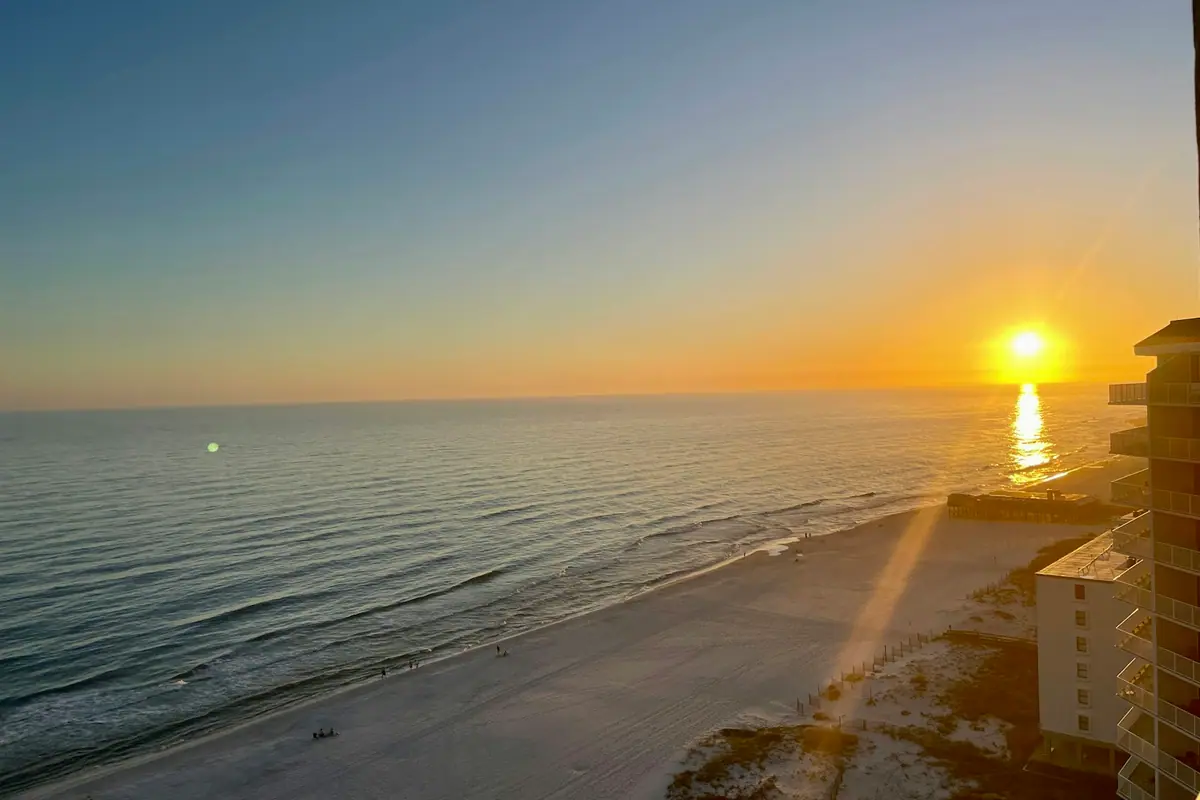 The sun going down over a quiet beach with a single low building along the shore